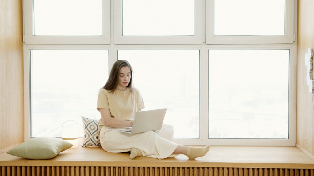 Une femme assise sur le rebord d’une fenêtre utilisant un ordinateur portable pour travailler sur un exemple de politique rh.