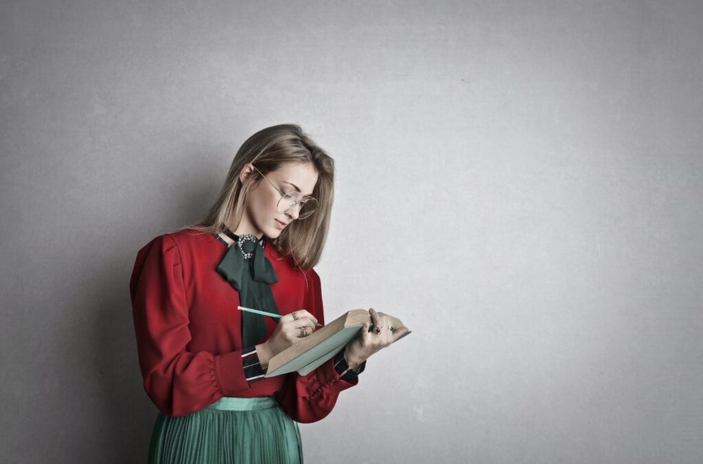 Une jeune femme écrivant dans un cahier lors d'une expérience contre un mur gris.