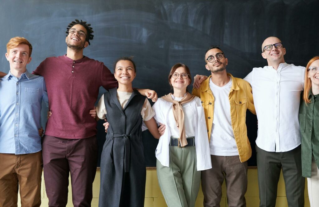 Un groupe diversifié de six personnes font la queue, souriant et serrant les bras devant un tableau, illustrant une forte fidélisation des employés.