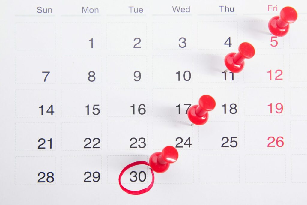 Une page de calendrier avec des punaises rouges marquant les vendredis et un cercle autour du 30e jour du mois, idéale pour suivre les dates d'entretien à l'aide d'ATS ou d'un logiciel de recrutement pour une gestion simplifiée des entretiens ATS.