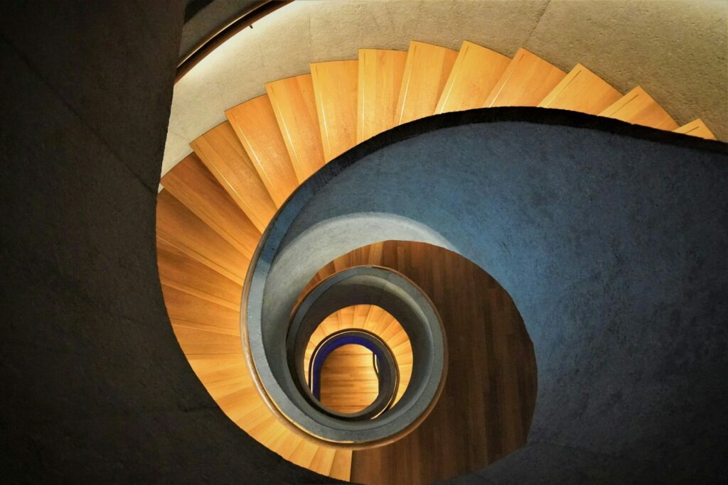 Escalier en colimaçon avec marches en bois et rampes en béton, vu de dessus, formant des motifs circulaires concentriques - idéal pour inspirer les espaces où vous prévoyez l'entretien ou rationalisez la gestion des entretiens ATS.