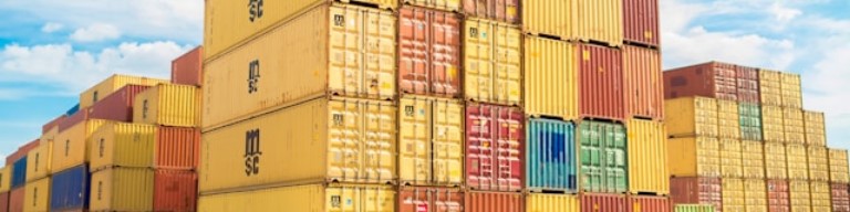 Des piles de conteneurs maritimes multicolores sont disposées en plein air sous un ciel partiellement nuageux, soulignant le rôle vital du transport et de la logistique dans les solutions modernes de recrutement comme des ATS. Photo qui symbolise le contexte d'un ATS recrutement pour améliorer l'expérience candidat