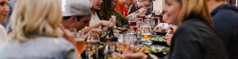 Un groupe de recruteurs assis autour d'une longue table dans un restaurant animé, dégustant de la nourriture et des boissons tout en engageant une conversation animée sur le choix d'un ATS. Image symbolisant l'intérêt d'un Logiciel de recrutement (ATS) pour améliorer l'expérience candidat