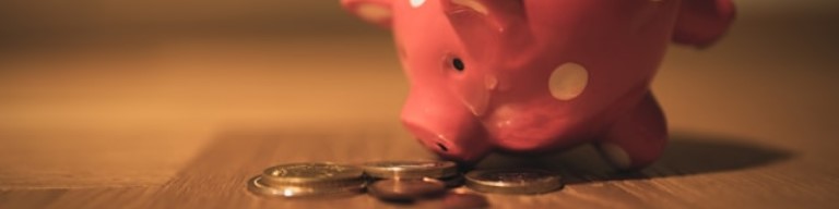 Une tirelire rose est posée sur le côté à côté d'une petite pile de pièces de monnaie assorties sur une surface en bois, suggérant les économies que vous pouvez réaliser en choisissant le bon logiciel recrutement ou la bonne solution ATS pour votre banque. Photo d'illustration : intérêt d'un ATS pour centraliser les offres et candidatures