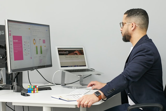 Un DRH travaille à un bureau équipé d'un écran d'ordinateur, d'un ordinateur portable, d'un bloc-notes et d'un Rubik's Cube. Des graphiques et des diagrammes relatifs au logiciel de recrutement sont affichés à l'écran. Photo pour symboliser : Comment centraliser les offres et candidatures dans La pharmacie, les biotechnologies et l'industrie de la santé