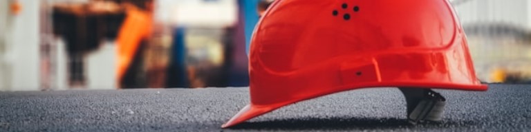 Casque de sécurité rouge posé sur une surface plane sur un chantier de construction, symbolisant l'emploi et la sécurité dans l'industrie, avec un équipement industriel flou en arrière-plan. Illustration des avantages d'un logiciel de recrutement (ATS) dans le secteur industriel pour améliorer l'expérience candidat