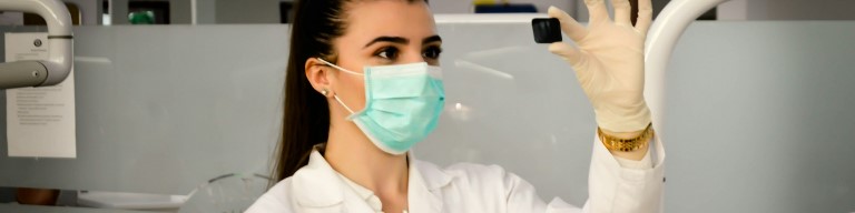 Une femme portant une blouse, un masque et des gants brandit un petit objet noir dans un laboratoire, illustrant la précision, à l'instar d'un recruteur utilisant ATS logiciel de recrutement pour une sélection précise des candidats. Photo illustrant l'utilisation d'un ATS pour améliorer l'expérience candidat dans le secteur de la santé