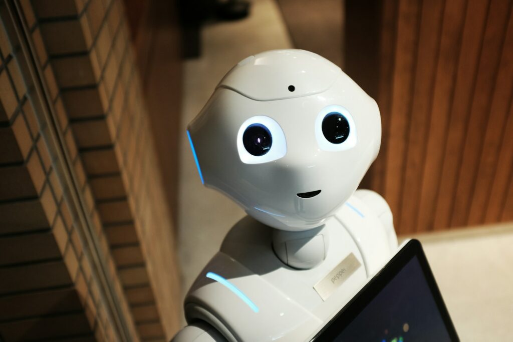 Un robot humanoïde blanc aux yeux lumineux se tient à l'intérieur, près d'un mur en briques, tenant un écran devant lui, et présentant une interface innovante de chatbot RH pour le site « carrière ».