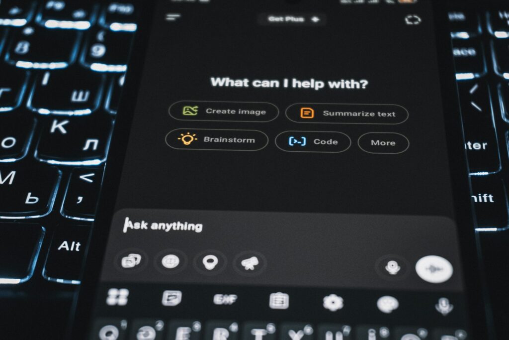 L'écran d'un smartphone affiche l'interface d'un chatbot basé sur l'IA, proposant des options telles que « Créer une image », « Résumer un texte », « Brainstorming » et « Codage » au-dessus d'un clavier rétroéclairé, illustrant ainsi comment l'IA interactive peut aider à définir des besoins spécifiques ou à renforcer les stratégies de marque employeur.